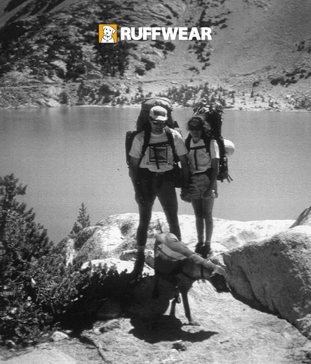 Two humans stand with their dog in 1994, the year Ruffwear began.