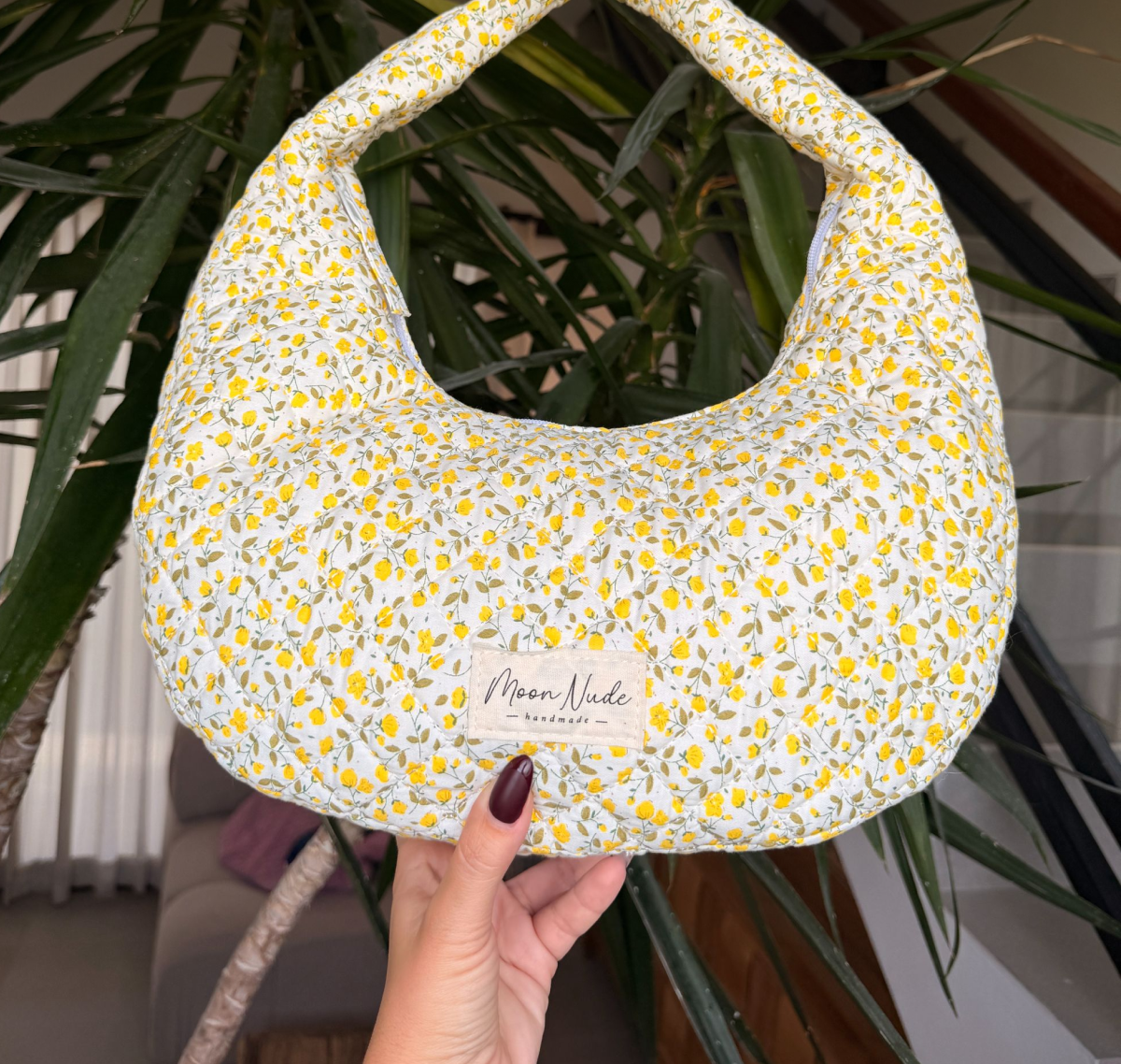 A floral patterned bag with a yellow and white design, held in front of a plant.