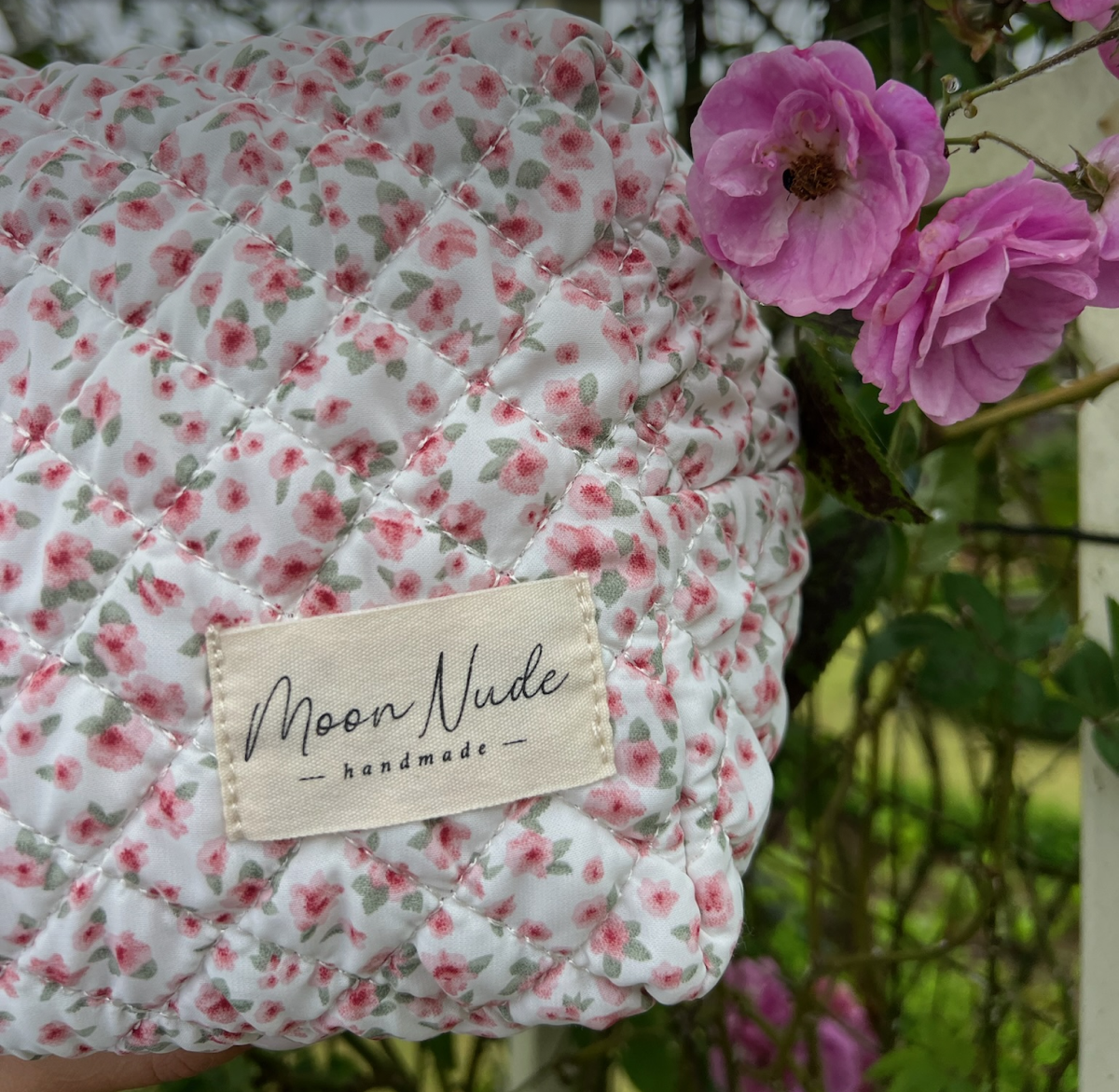 Close-up of a floral quilted fabric with a tag reading 'Moon Nude - handmade' and pink flowers.