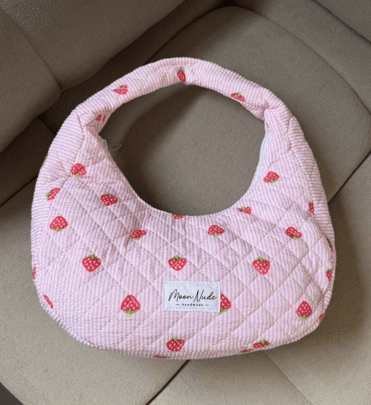 A pink quilted handbag with small strawberry patterns.