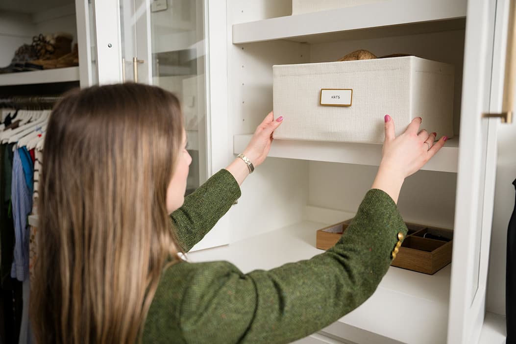 A woman placing a labeled Oxford Bin on a closet shelf