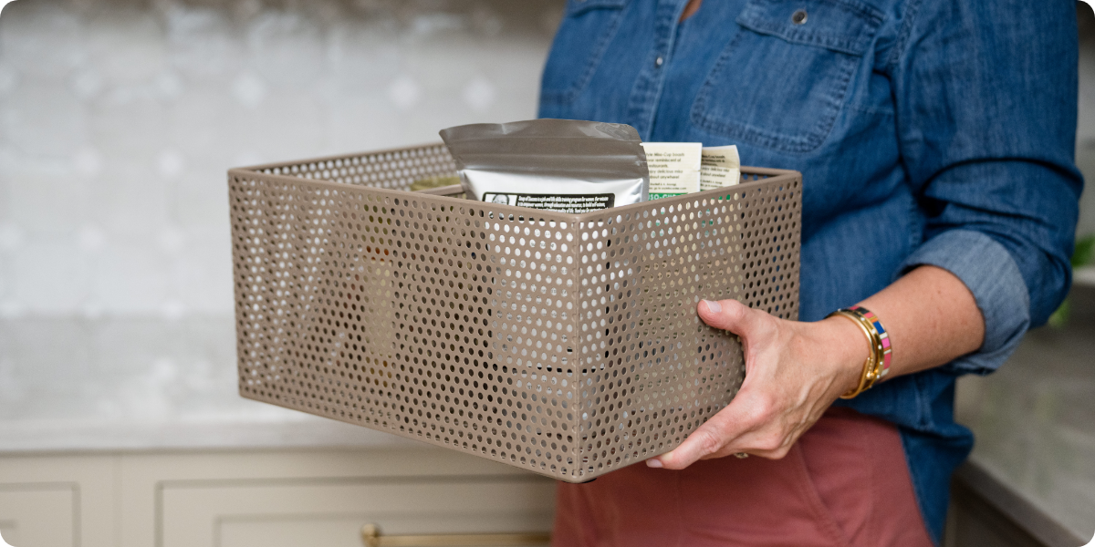A person holding a perforated basket with pantry items inside.