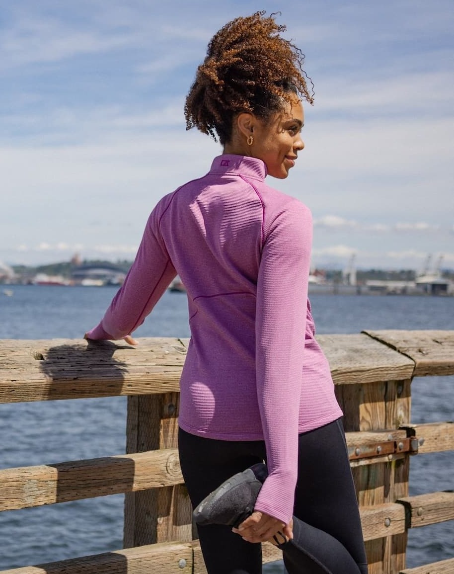 Woman wearing pink Peshastin recycled half zip and stretching on the pier | Shop Layering