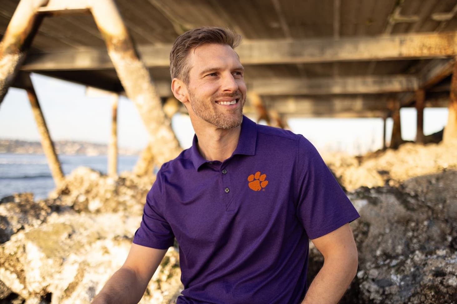 Man sitting on the beach wearing a purple Clemson Tigers Cutter & Buck Polo Shirt