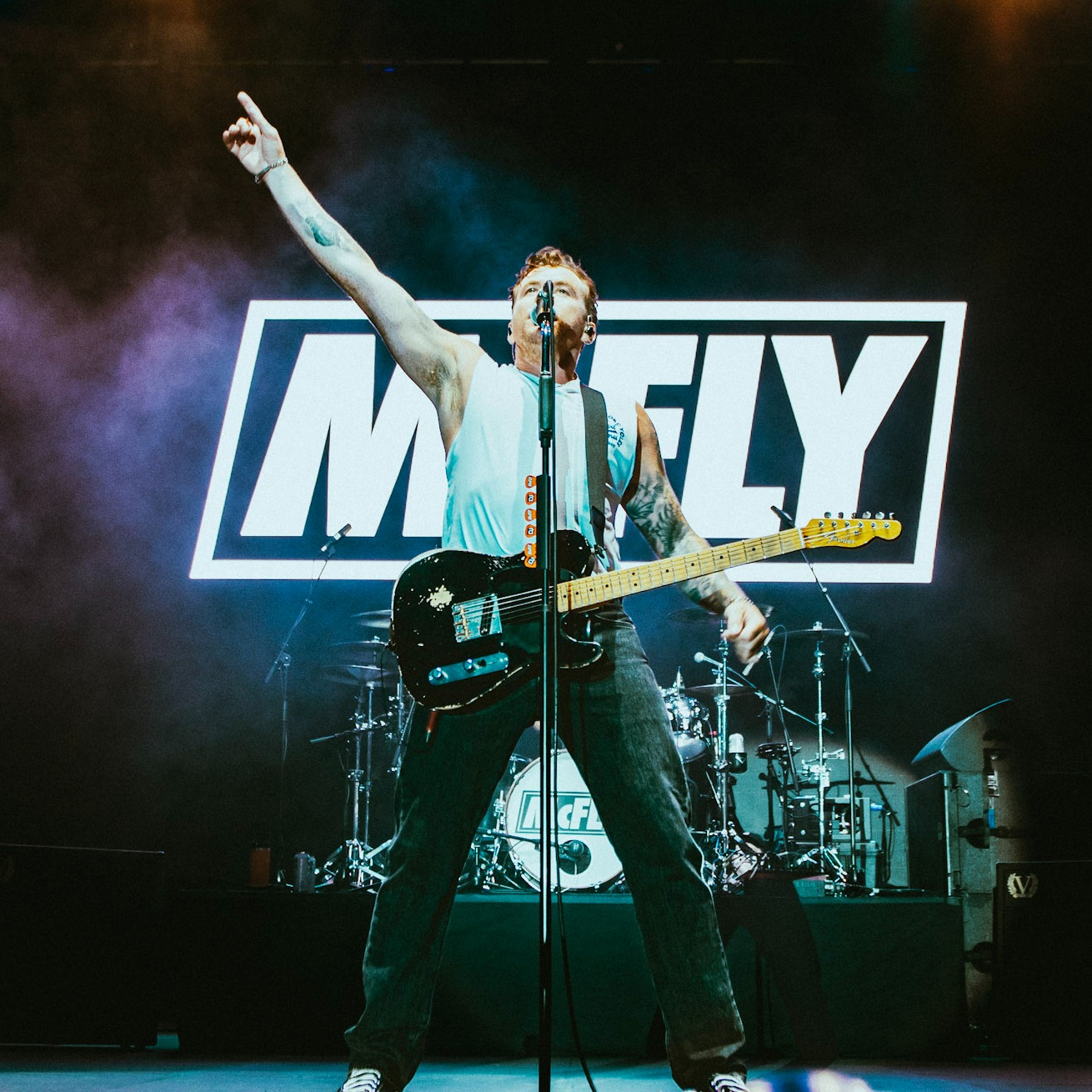 Danny Jones facing the camera showing off the GT tee whilst on stage with the McFly logo in the background
