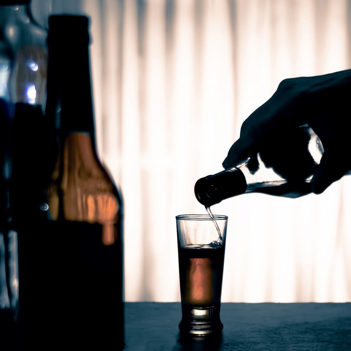 shadowed hand pouring liquor into a shot glass with bottle in foreground