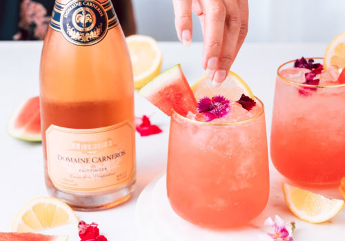 Bottle of Domaine Carneros and two stemless glasses of a cocktail