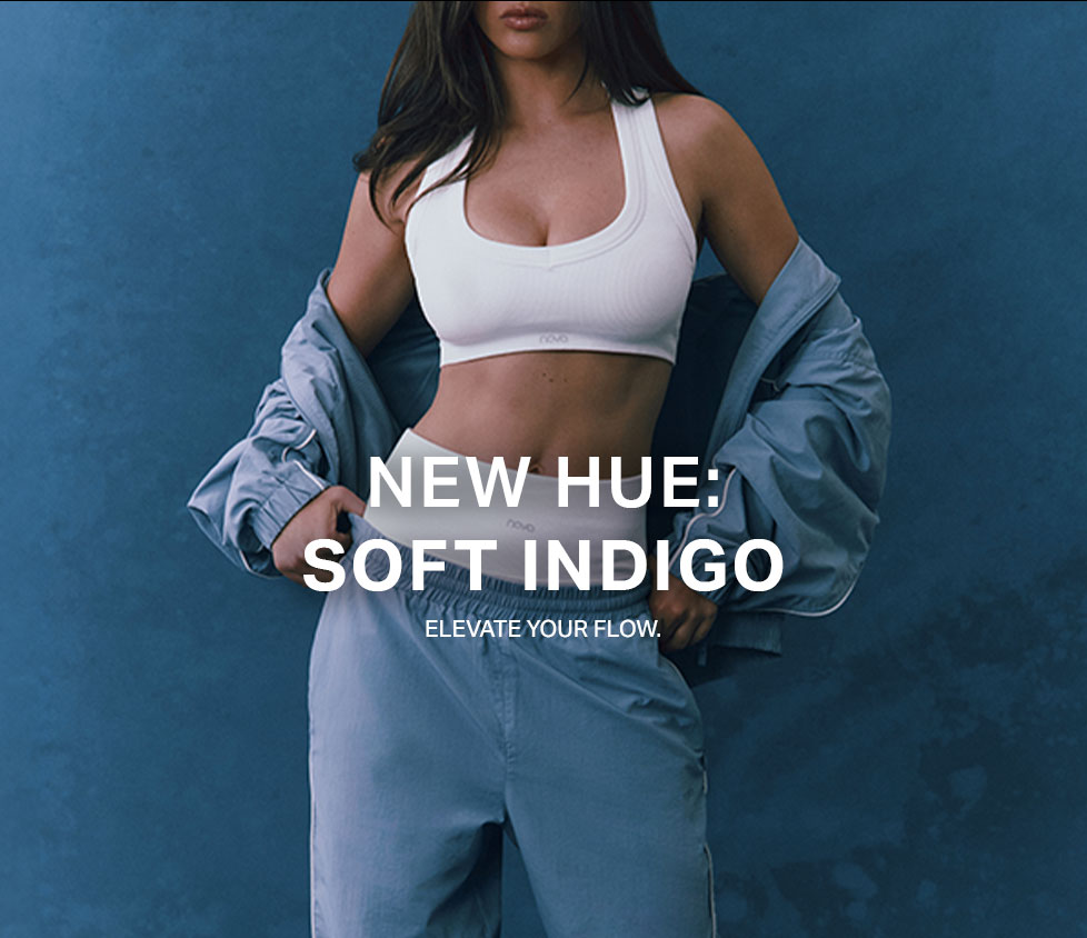 Ribbed white sports bra, soft indigo track pants, and matching jacket on a person. Showcases the new Soft Indigo activewear collection.