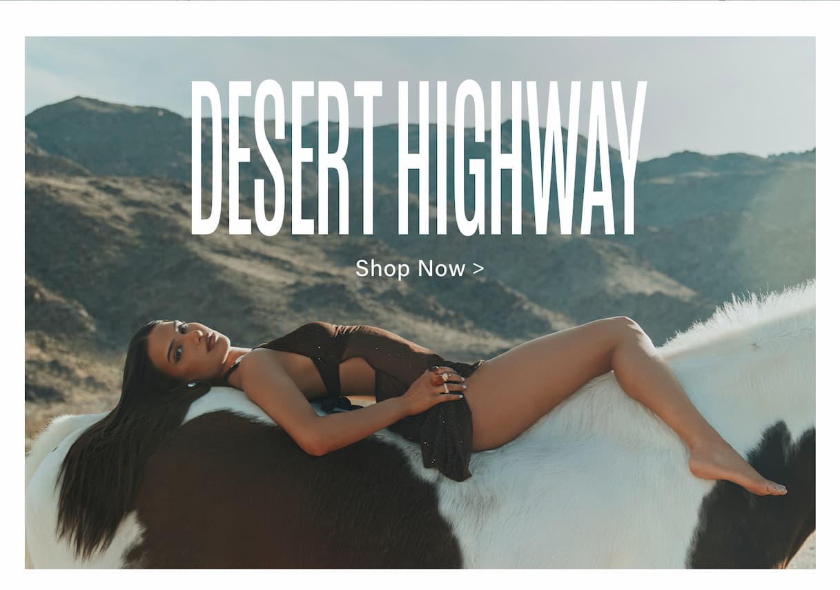 Woman in a shimmering brown dress reclines on a black & white pinto horse with desert hills. Shop the new Desert Highway collection.