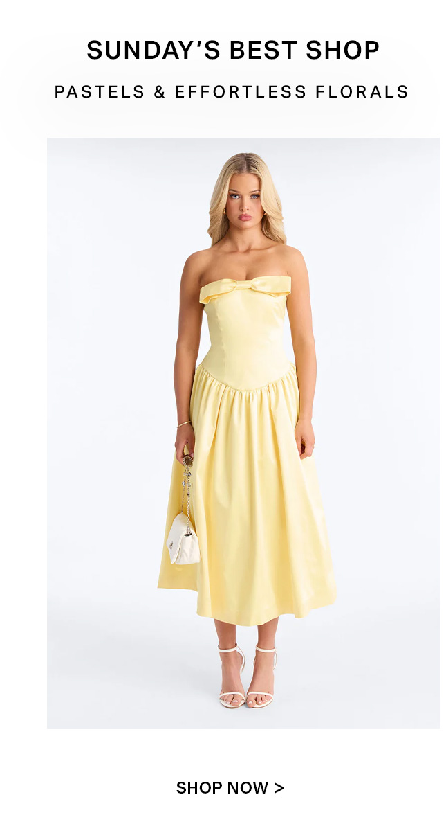 Blonde woman in pastel yellow strapless bow midi dress, holding white bag & wearing heels. For Sunday's Best effortless collection.