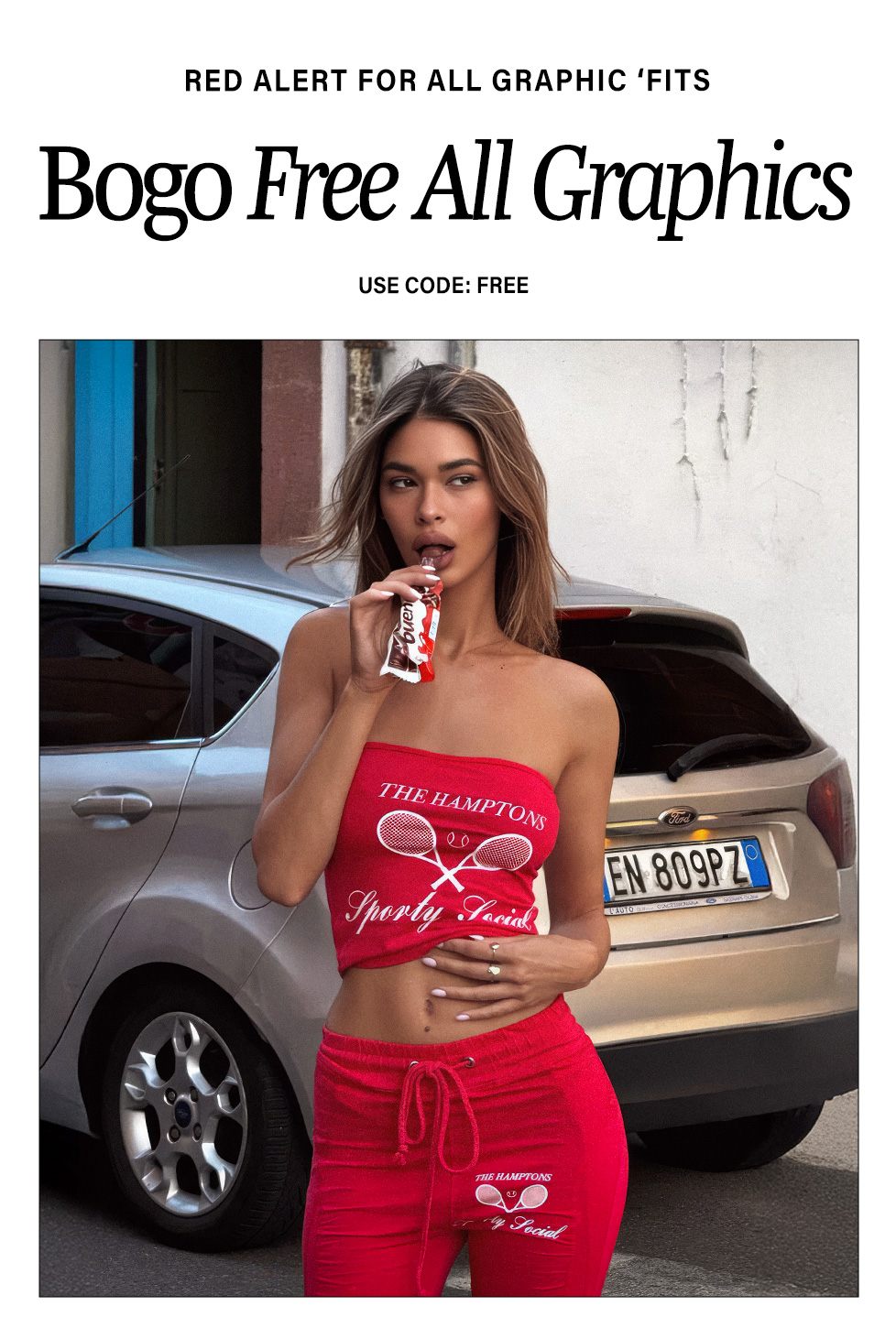 Stylish woman in a red strapless graphic top and matching sweatpants with tennis rackets, enjoying a treat. Promotes BOGO Free graphic apparel.