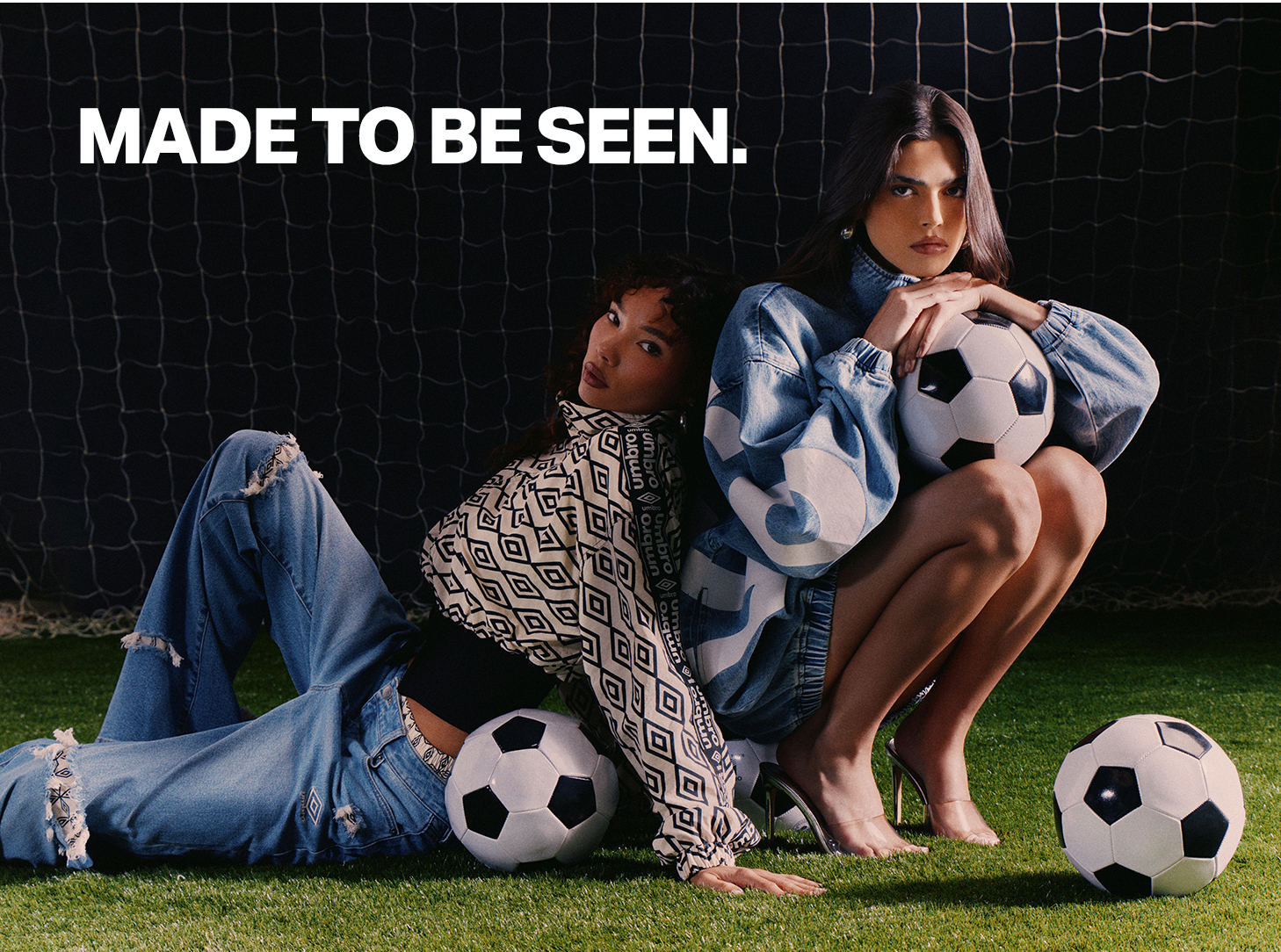 Umbro women's fashion: 2 models in streetwear (denim, patterned jacket) with soccer balls on turf. MADE TO BE SEEN.