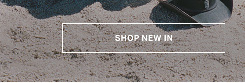 White "SHOP NEW IN" text in a bordered box over a light brown, sandy textured background, directing to discover new arrivals.
