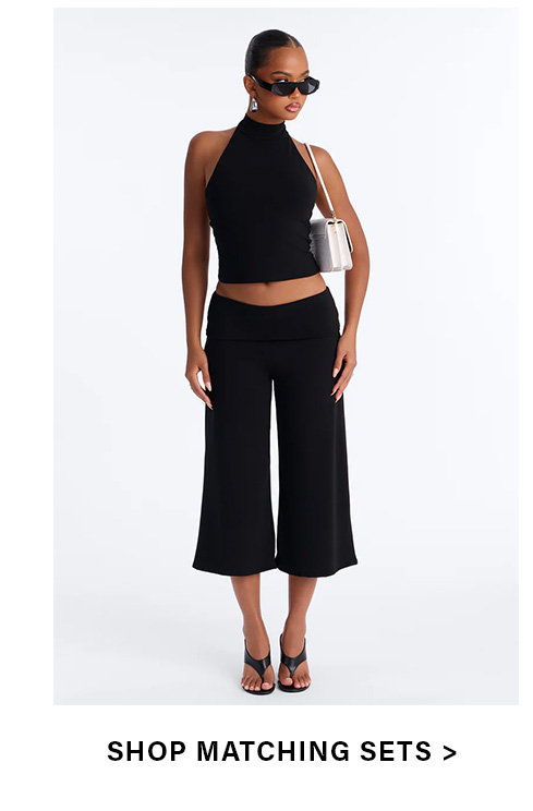 Chic black halter crop top & wide-leg cropped pants matching set for women. Stylish two-piece outfit with sunglasses & shoulder bag.