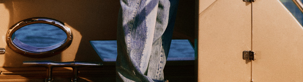 Blue jeans on a yacht. Brass porthole overlooks blue ocean. Nautical travel, denim fashion, luxury leisure.