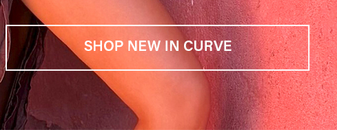 Close-up of an leg and dark garment against a textured coral background, with a 'Shop New In Curve' button promoting new plus-size fashion.