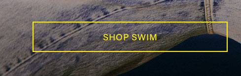 Close-up of a person's leg in textured gray-blue denim, partially submerged in dark water, with yellow 'SHOP SWIM' text. Discover our swim collection.
