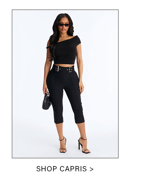 Stylish woman models a black off-shoulder crop top, belted black capri pants, and high heels against a white background. Shop new capris fashion.