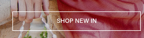 "SHOP NEW IN" text overlay on a hand holding a delicate pearl bracelet against flowing red fabric. Explore our new arrivals and latest fashion collection.