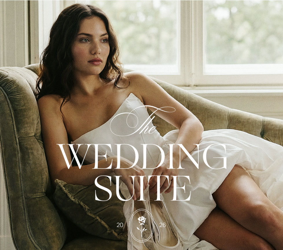 Elegant woman in a strapless white wedding gown reclines on a green sofa, holding shoes. Announcing the elegant new Wedding Suite bridal collection.