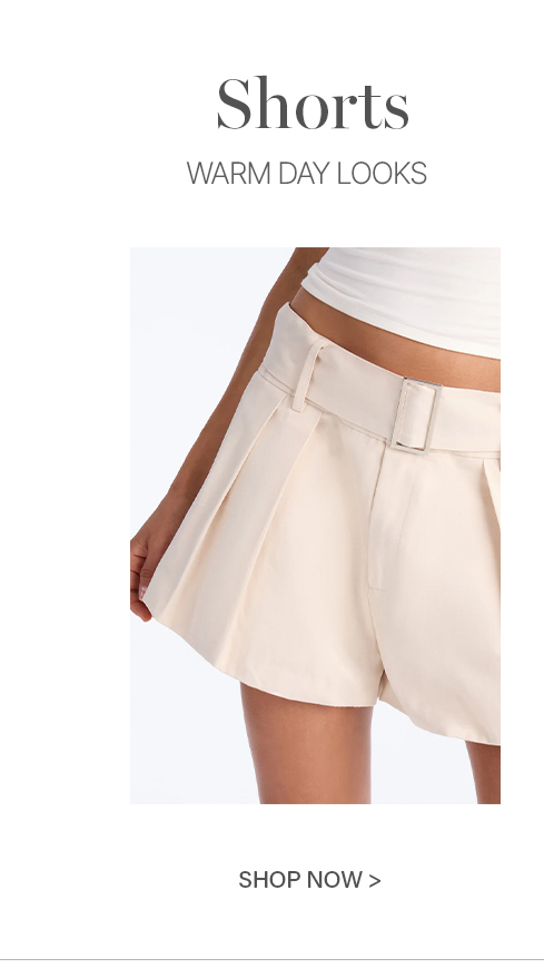 Cream pleated shorts with a rectangular buckle belt, paired with a white crop top, highlighting warm weather fashion. Shop stylish shorts.