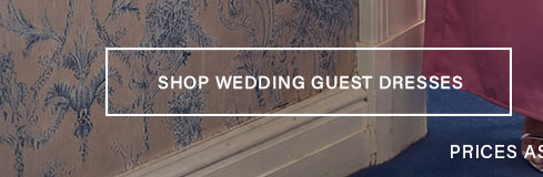 Partial view of a person in a flowing magenta dress. The image features blue patterned wallpaper and blue carpet, with text "SHOP WEDDING GUEST DRESSES."