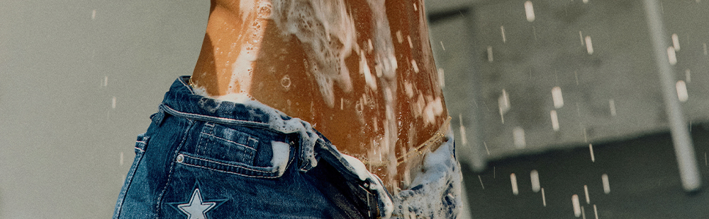 Tanned torso with suds & water, wearing unzipped blue denim jeans with a white star. Refreshing shower or body care.