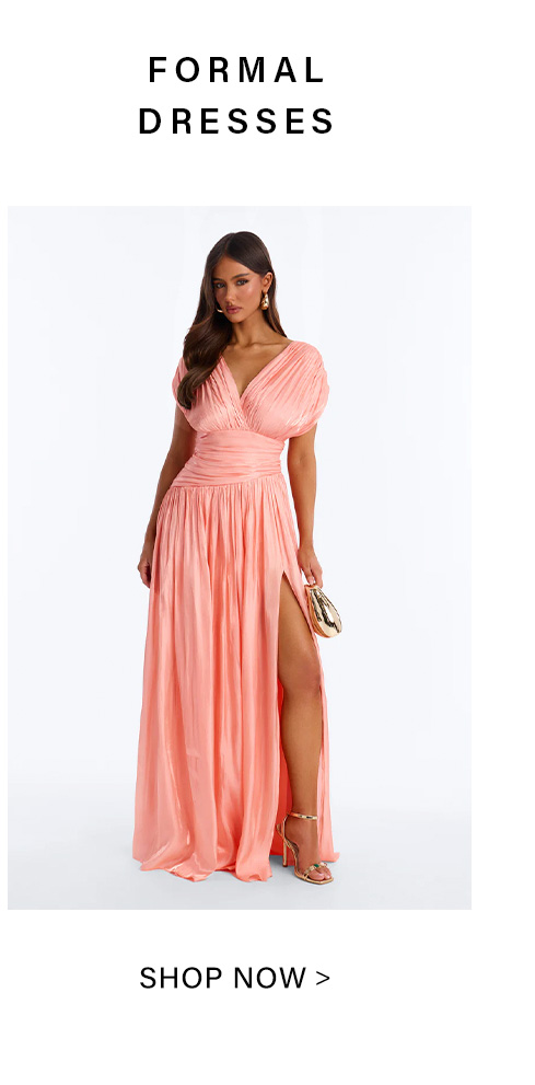 Elegant woman in a flowing coral formal dress with a ruched V-neck and high slit, holding a gold clutch. Shop the latest formal dresses.