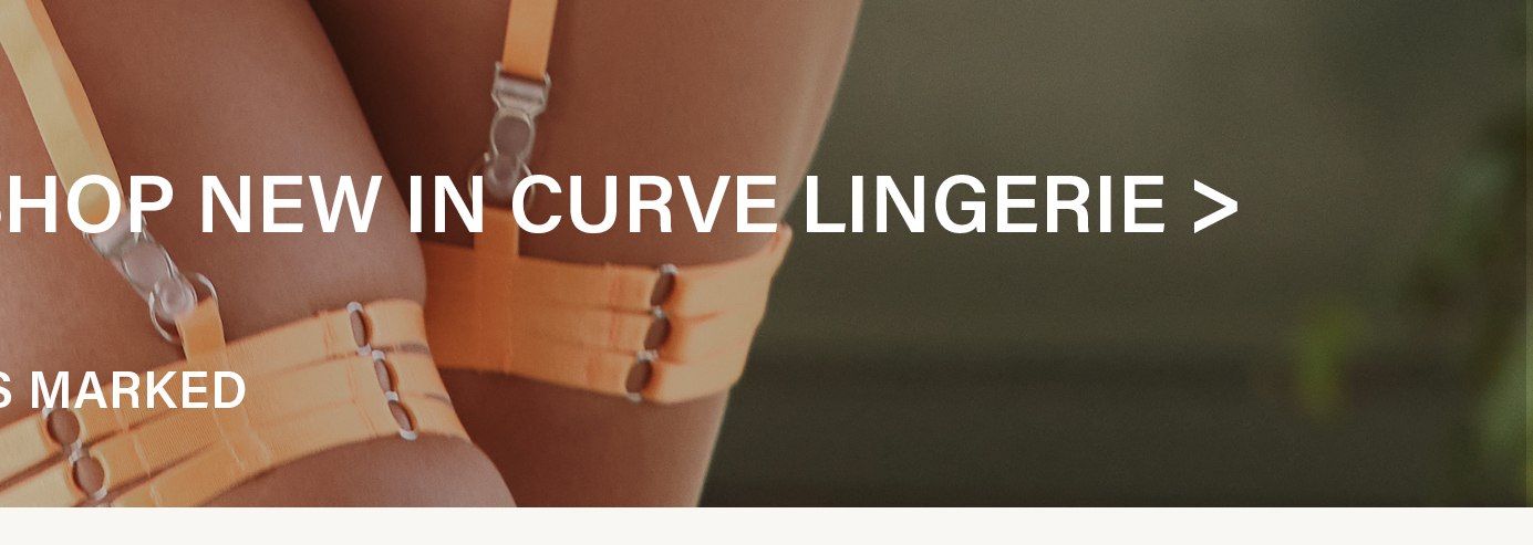 Close-up of upper thighs wearing bright orange garter lingerie with silver hardware, against a dark background. Shop new curve lingerie.