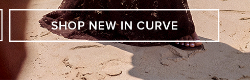 SHOP NEW IN CURVE banner: Woman's foot in sandal on sandy beach, promoting new arrivals for women's plus size fashion & curve clothing.