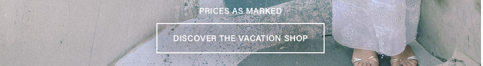 Woman's feet in gold sandals and flowing white lace dress on gray ground. Discover the vacation shop for resort wear and summer style.