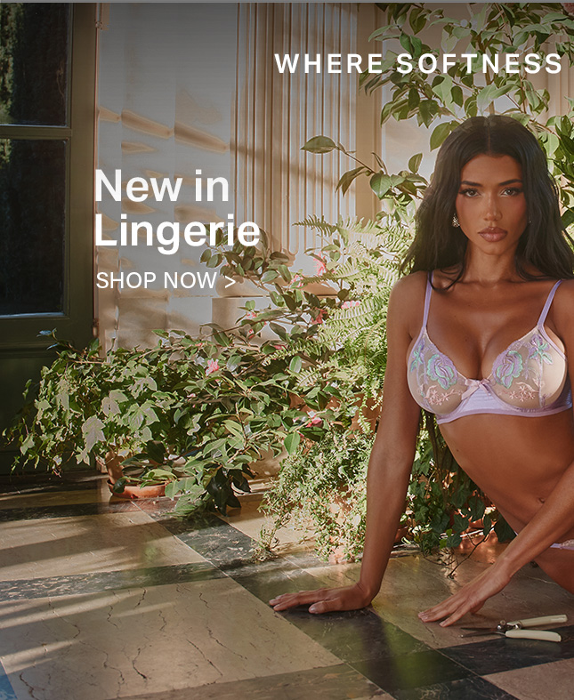 Woman modeling a new lavender floral embroidered bra, kneeling by lush green plants. Discover the new lingerie collection where softness meets style. Shop now.