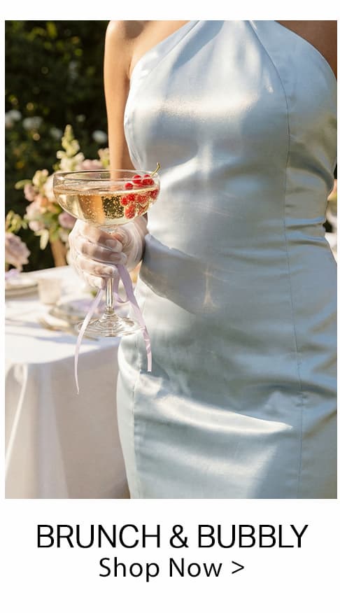Pale blue one-shoulder satin dress, perfect for brunch & bubbly, worn by a person holding a sparkling cocktail with red berries outdoors. Explore event styles.