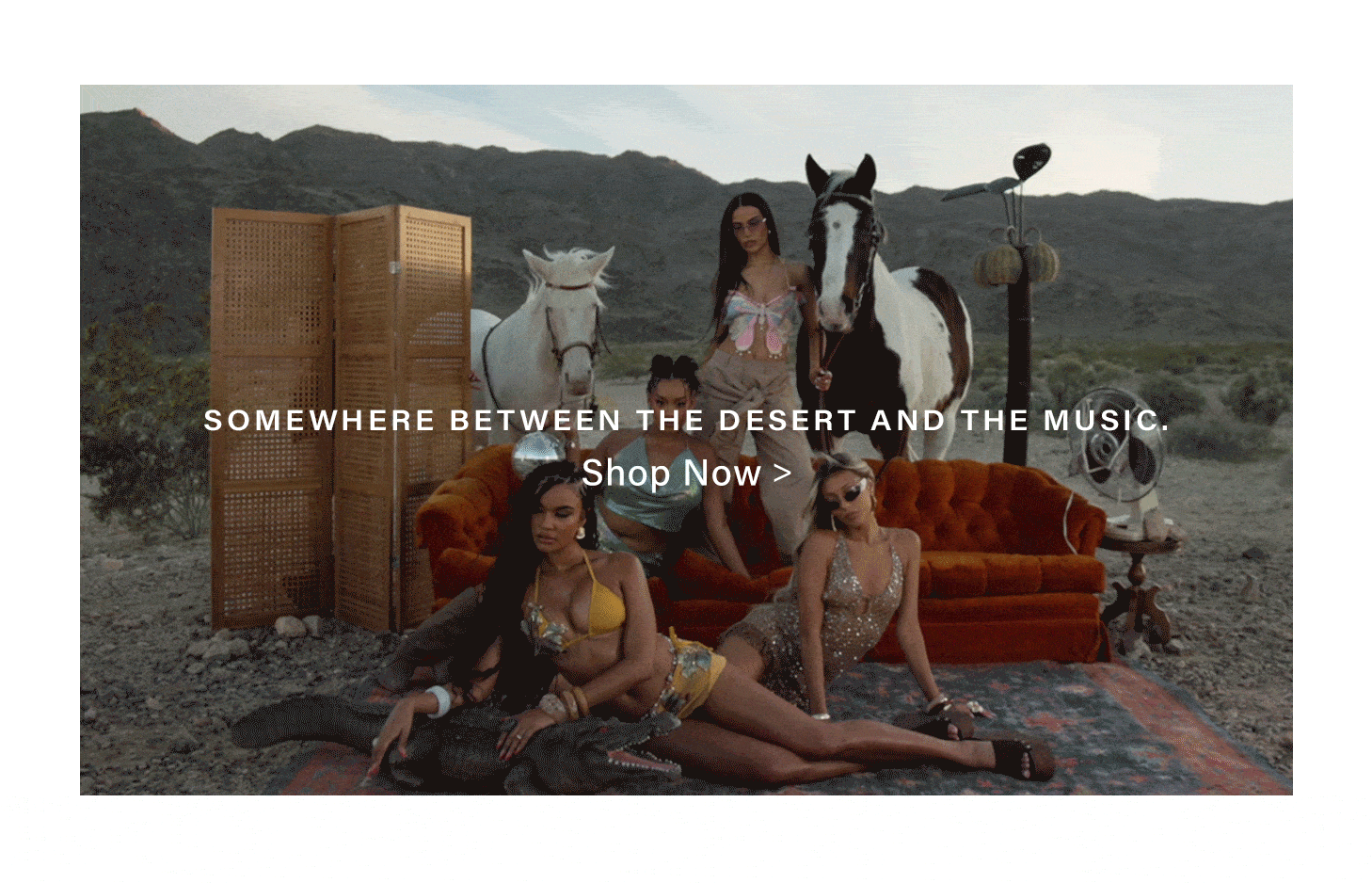 Colorful desert fashion collection: four models pose with two horses, an orange couch, and a fan in a vast desert landscape. Shop new styles.