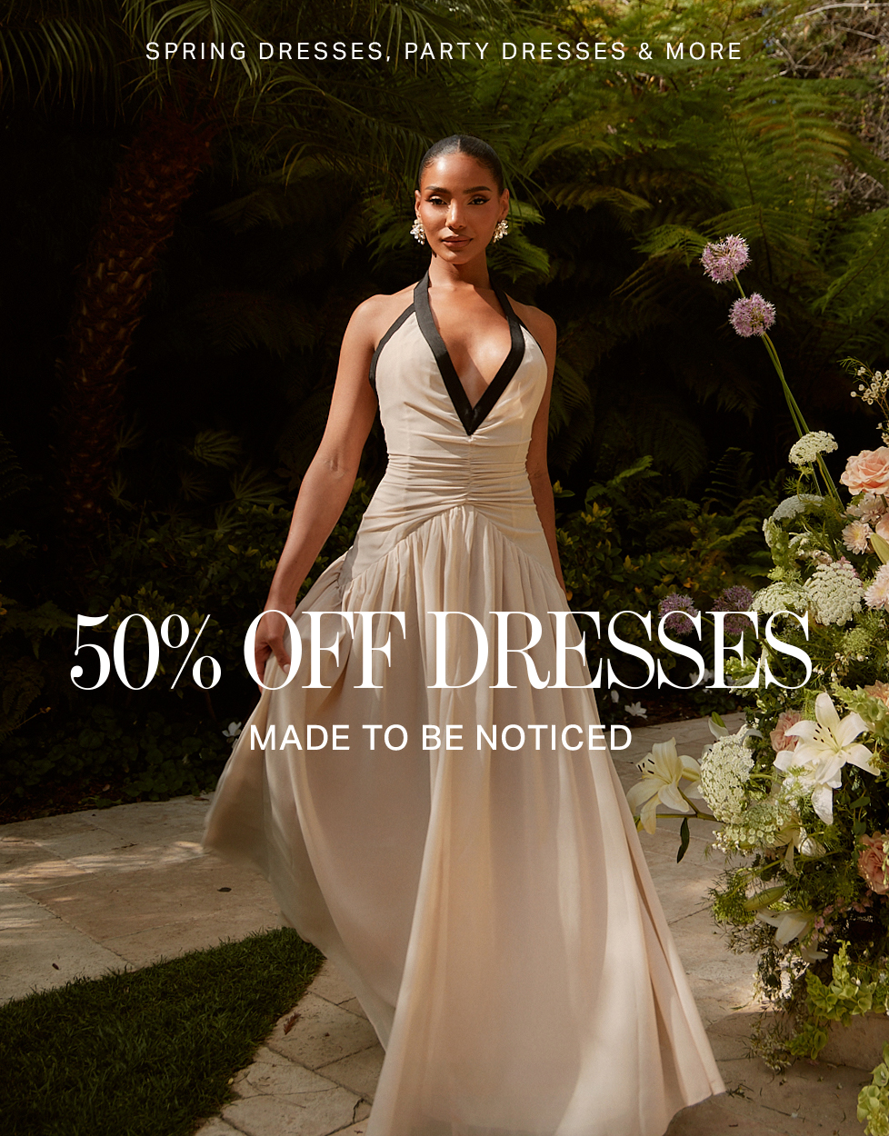 Elegant woman in a flowing beige halter dress with black trim amidst lush greenery, promoting 50% off spring and party dresses.