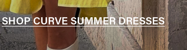Person in a vibrant yellow summer dress and light shoes, standing against a stone-like background. Shop our collection of curve summer dresses.