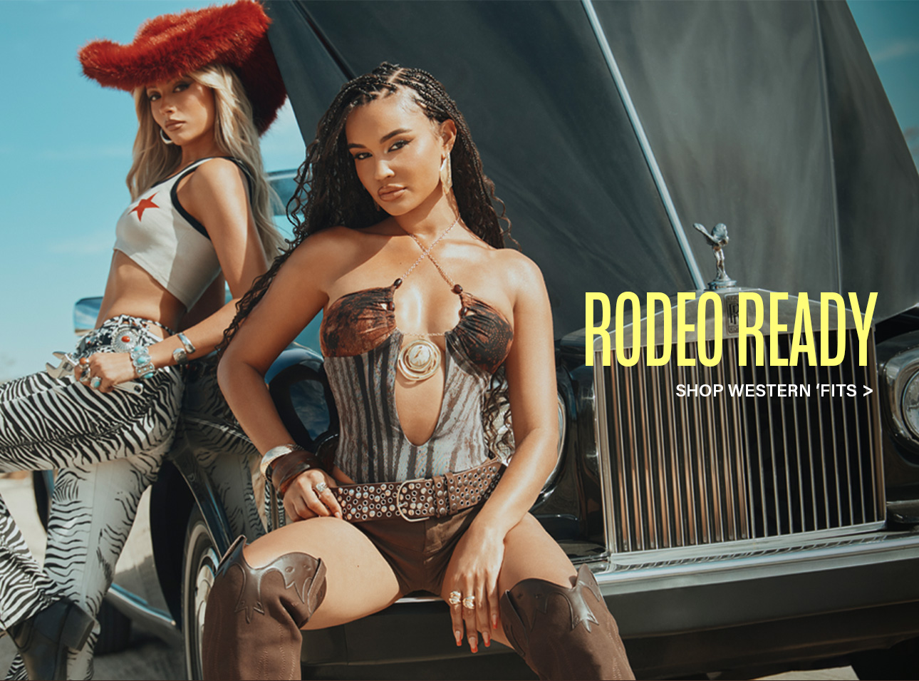 Two women in striking rodeo fashion pose with a black luxury car. One wears a red hat and zebra pants; the other, a patterned top and cowboy boots. Shop western wear.