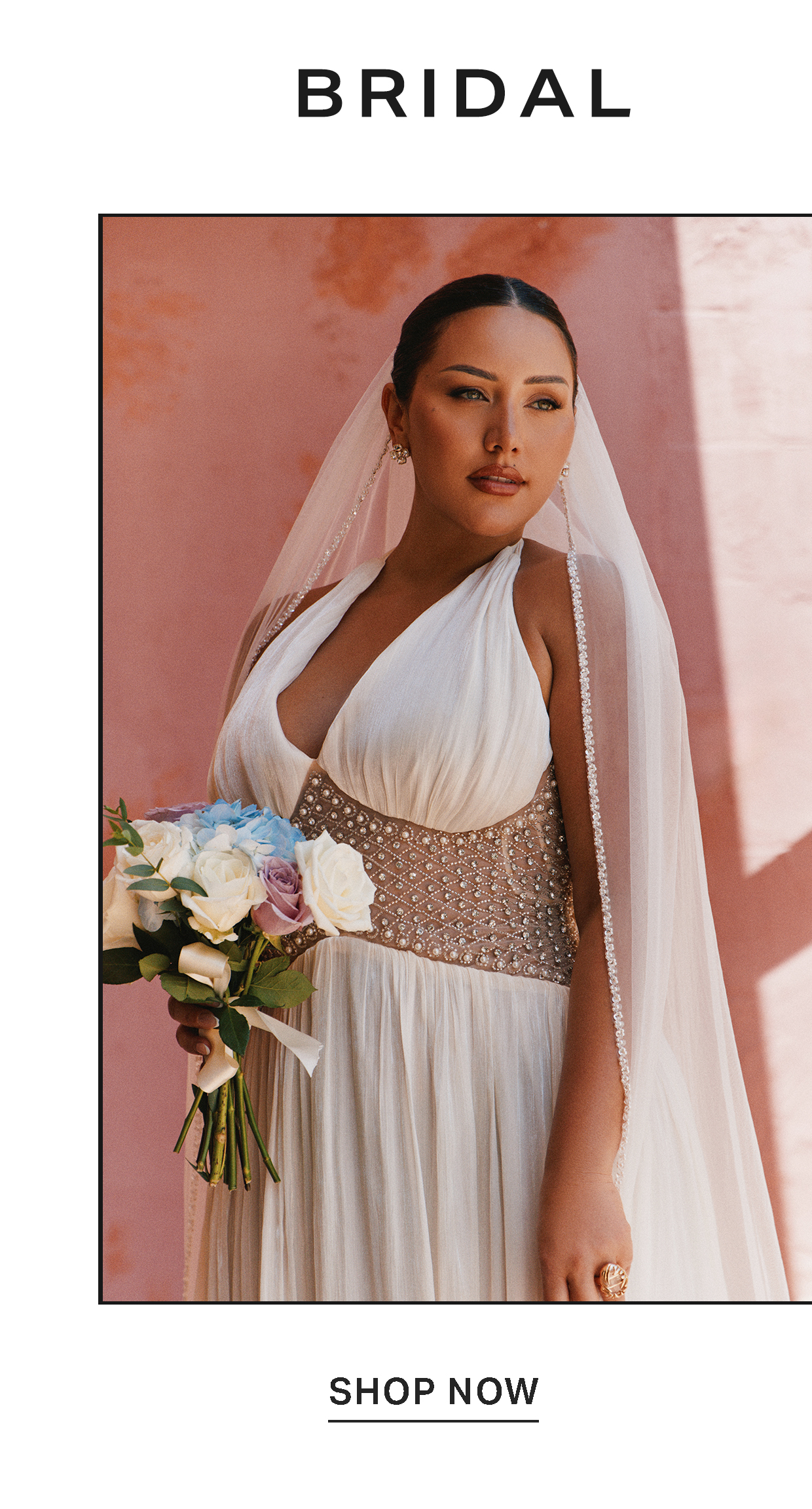 Bride in a white halter wedding dress with a beaded waist and veil holds a pastel bouquet against a pink wall to shop the bridal collection.