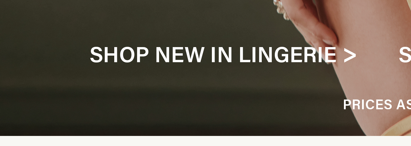 Close-up of a person's shoulder and arm, wearing a cream-colored lingerie item and subtle rings. Text "SHOP NEW IN LINGERIE" promotes the latest collection.