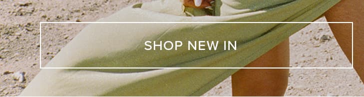 Close-up of a person wearing flowing sage green apparel on sandy ground, promoting new fashion arrivals. Discover our latest collection.