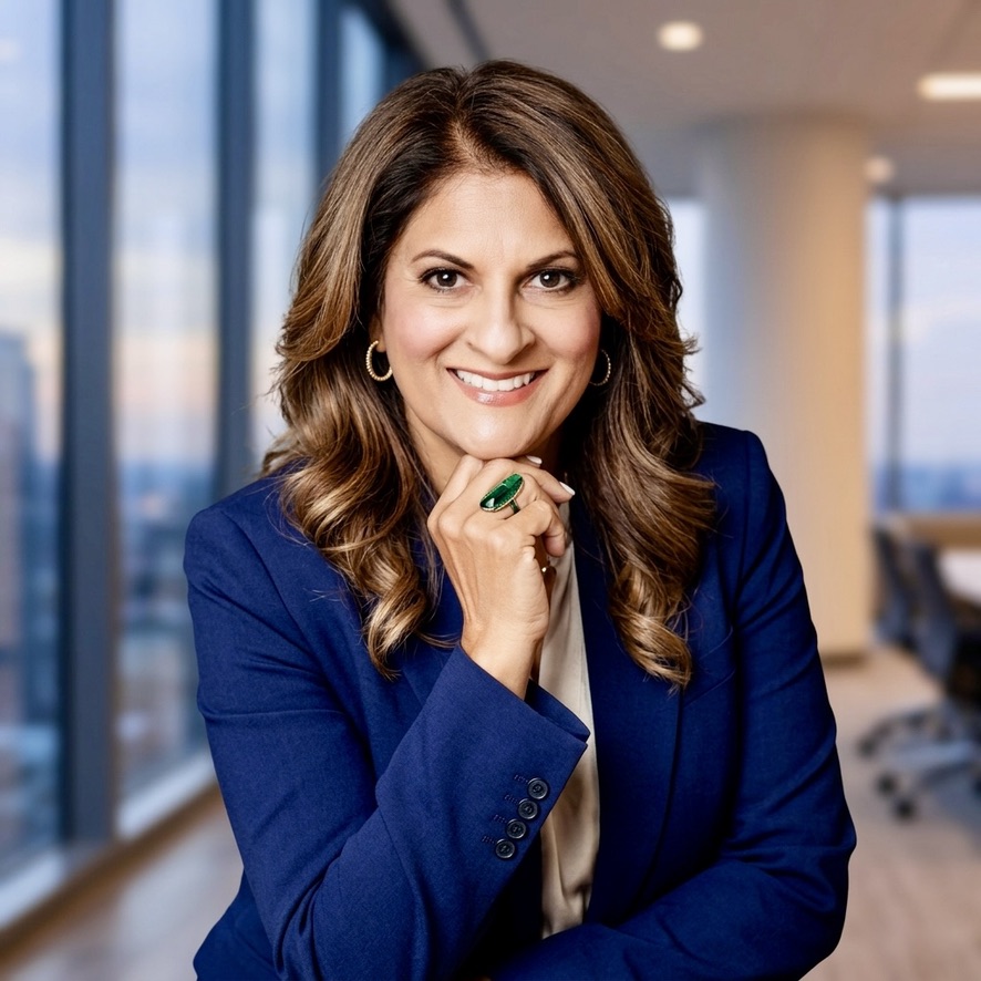 Ulka Wilson, smiling, in a navy blazer by an office window