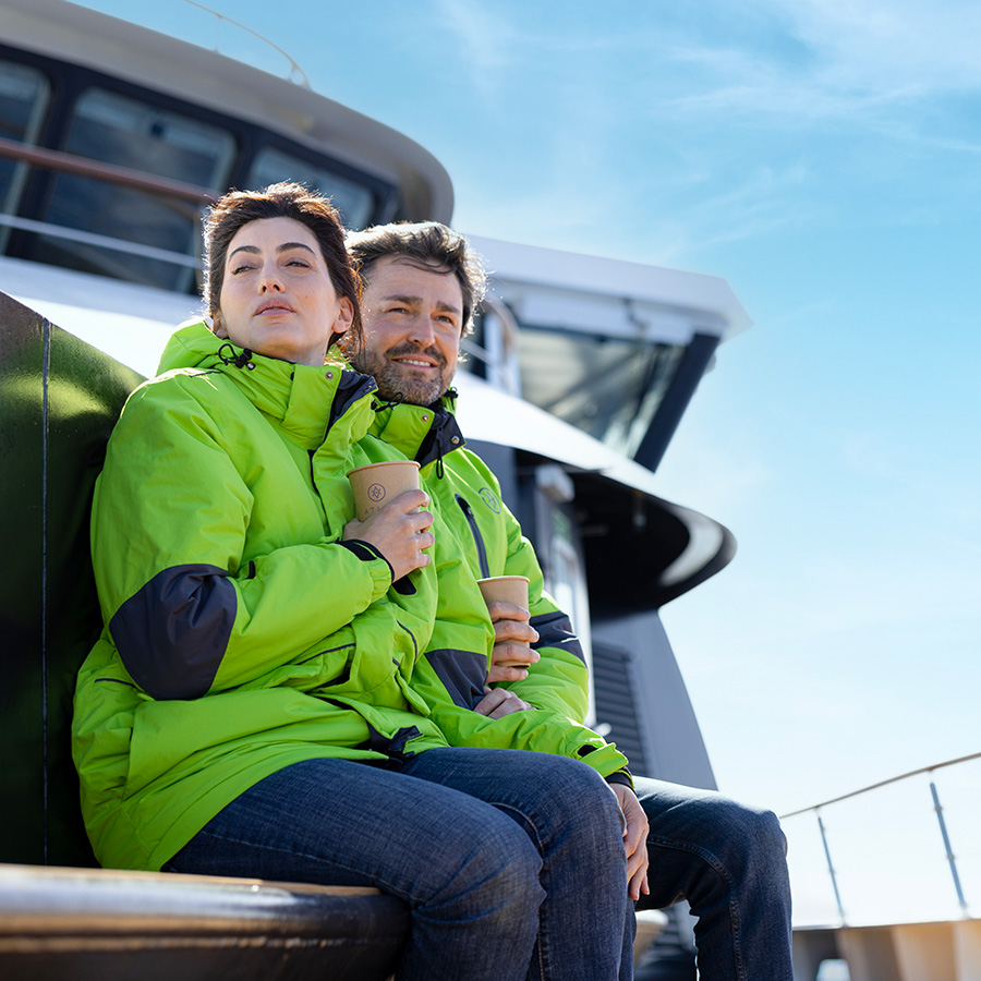 Couple sitting in their Atlas parkas on yacht deck