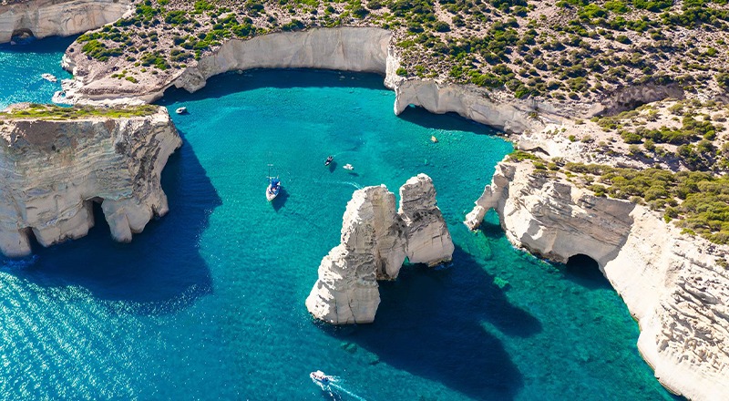 Small boats sailing amid cliffs and open water of Milos, Greece