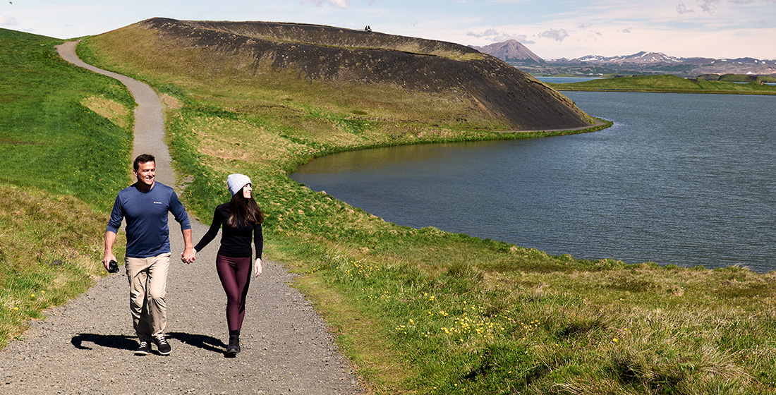 A man and woman holding hands walking down a seaside path in Akureyri, Iceland