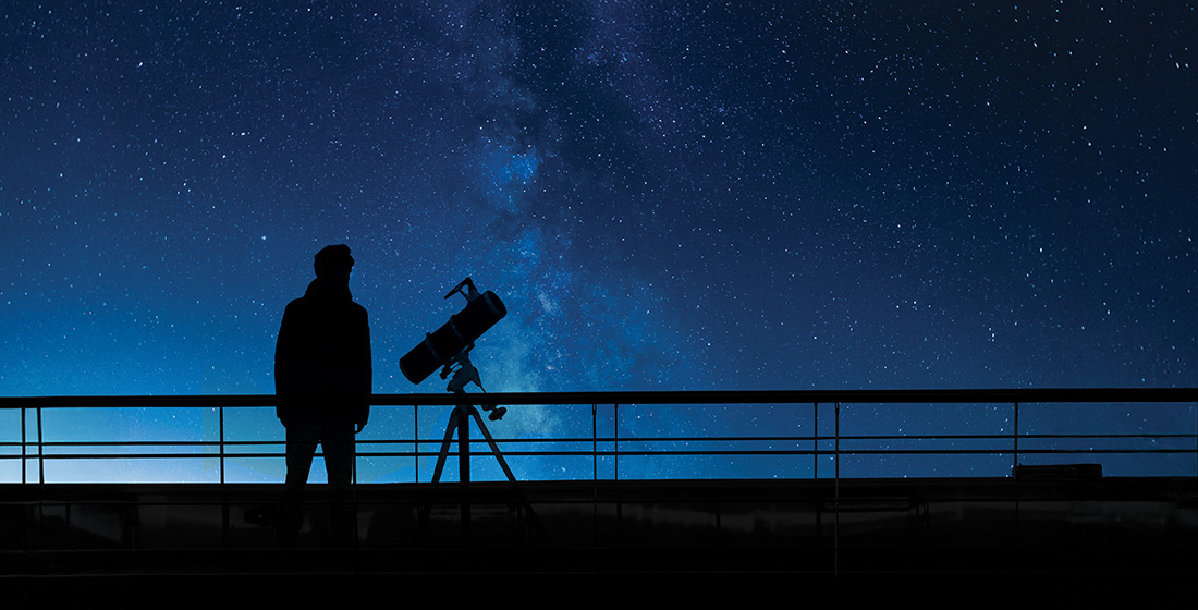 Astronomer gazing up at the night sky with a telescope aboard a yacht