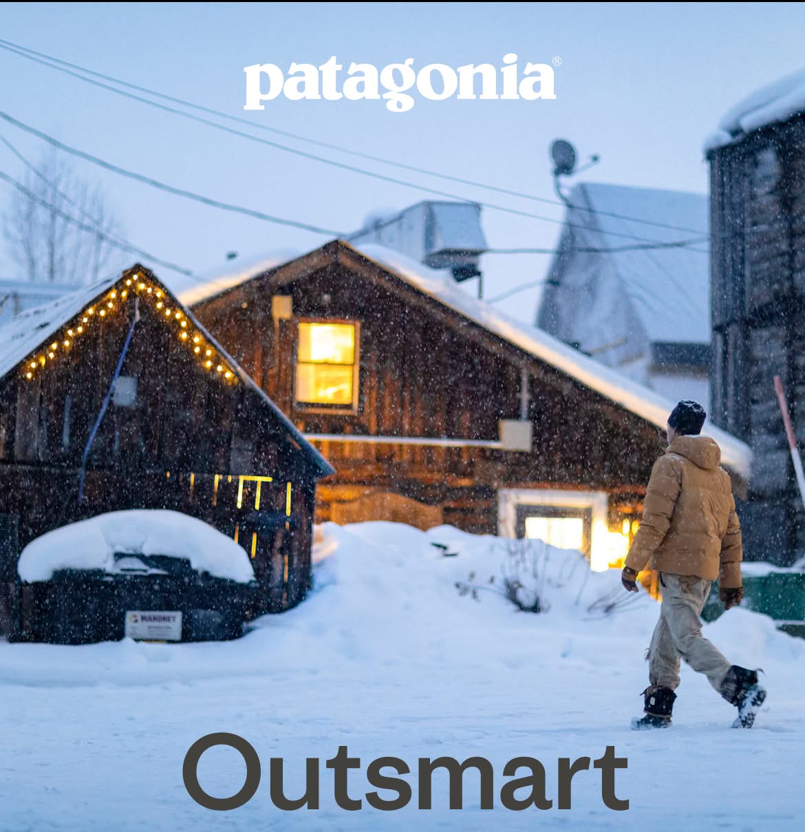 Patagonia. Outsmart the forecast. A person walks in the snow toward a wooden building.