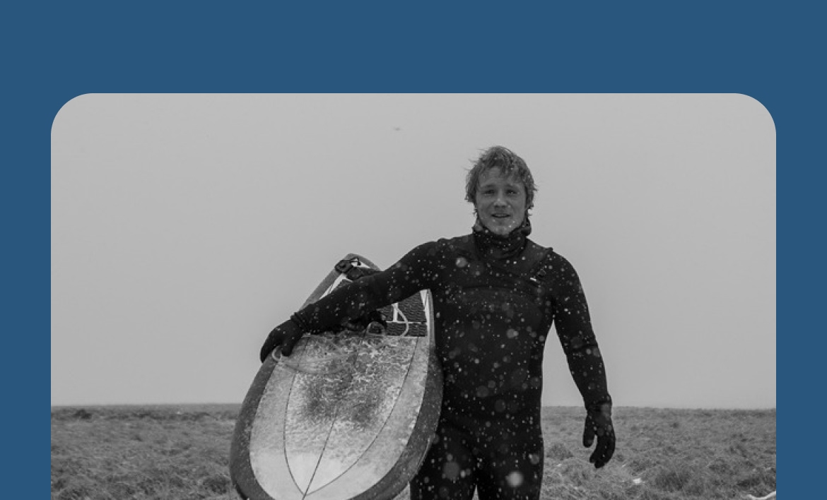 A person in a wetsuit holding a surfboard on a snowy day.