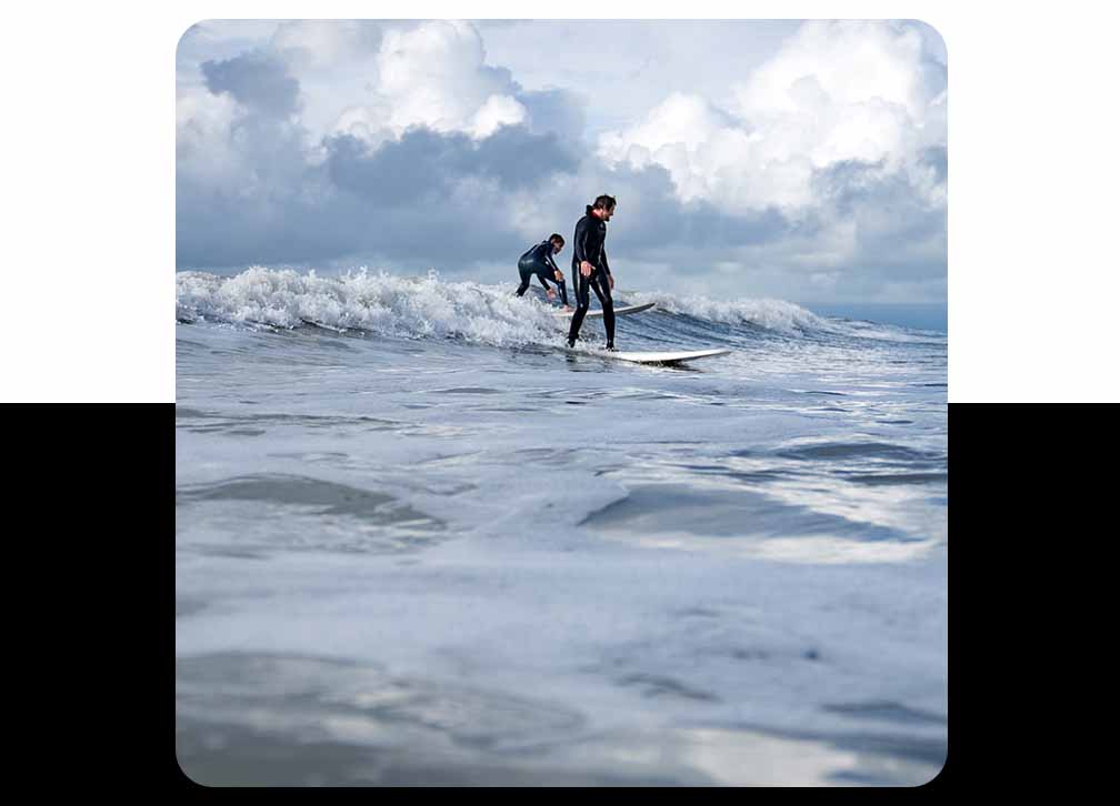 One adult and one young surfer ride the same small wave together.