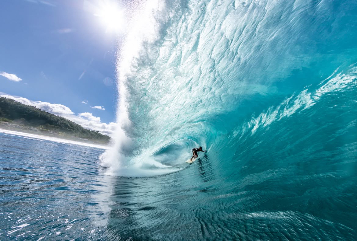 A surfer rides a huge barrel in pristine water on a sunny day.