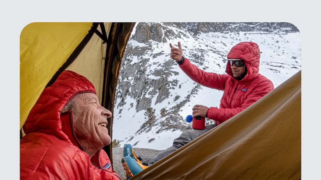 A climber peers out of the tent at their partner in the mountains. 